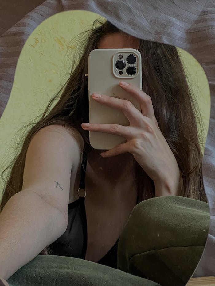 A young woman with long hair takes a mirror selfie using a smartphone, capturing her reflection.